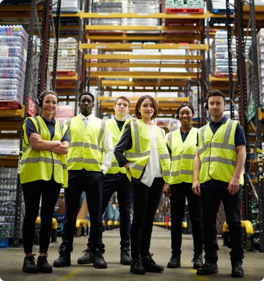 A group of individuals wearing safety vests gathered in a warehouse, engaged in discussion or inspection activities.